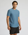 A man wearing a light blue crew-neck athletic t-shirt and black shorts, standing against a light gray studio background.
