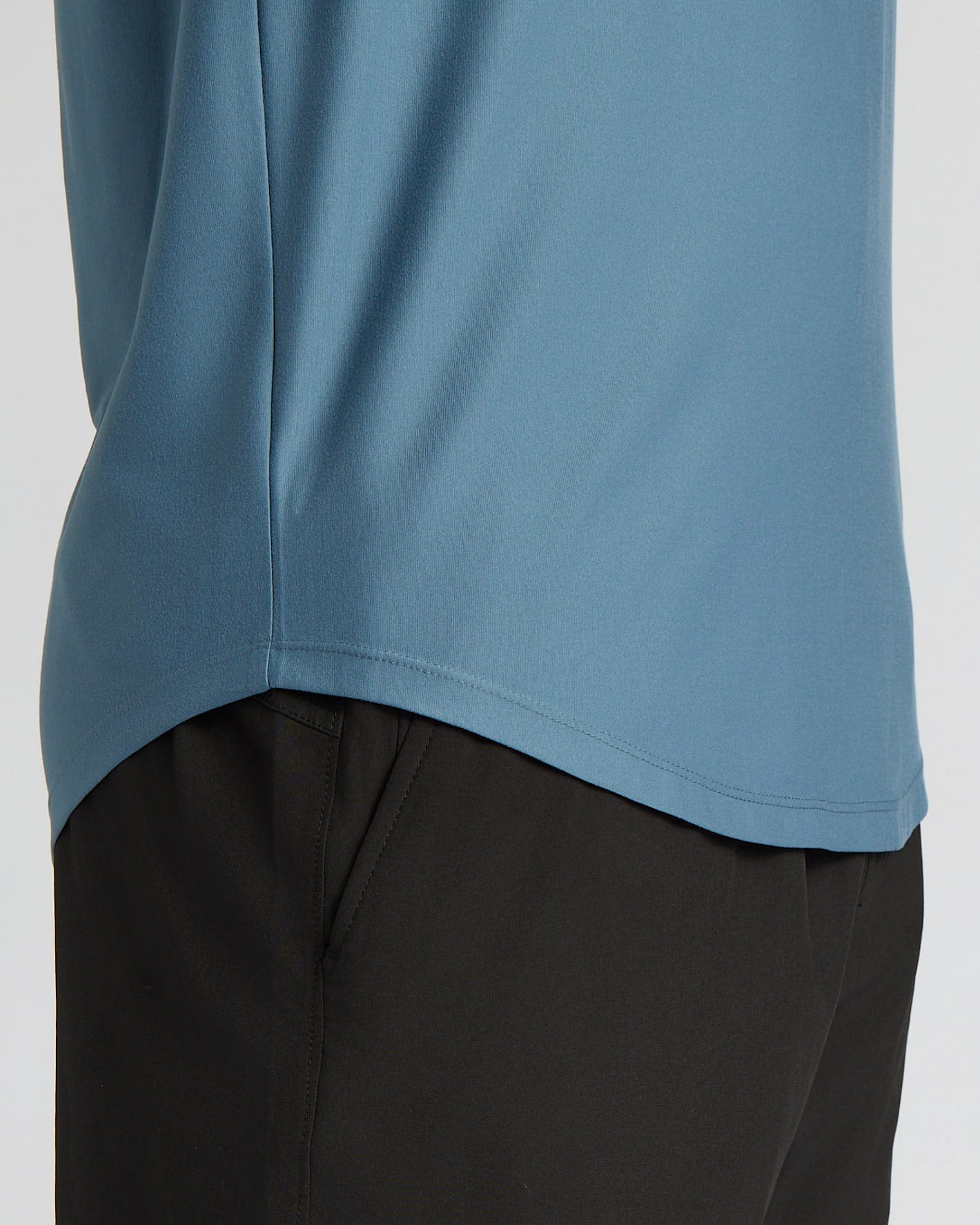 Close-up of a person wearing a dusty blue athletic top and black pants against a light gray background.