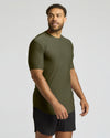 A man wearing a fitted short-sleeve athletic t-shirt in olive green, paired with black shorts, photographed against a light gray studio background.