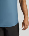 Close-up of a person wearing a dusty blue athletic t-shirt and black shorts against a light gray background.