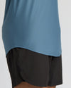Close-up of a person wearing a dusty blue athletic top and black athletic shorts against a light gray studio background.