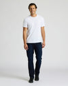 Man wearing a white t-shirt and dark jeans on a plain background