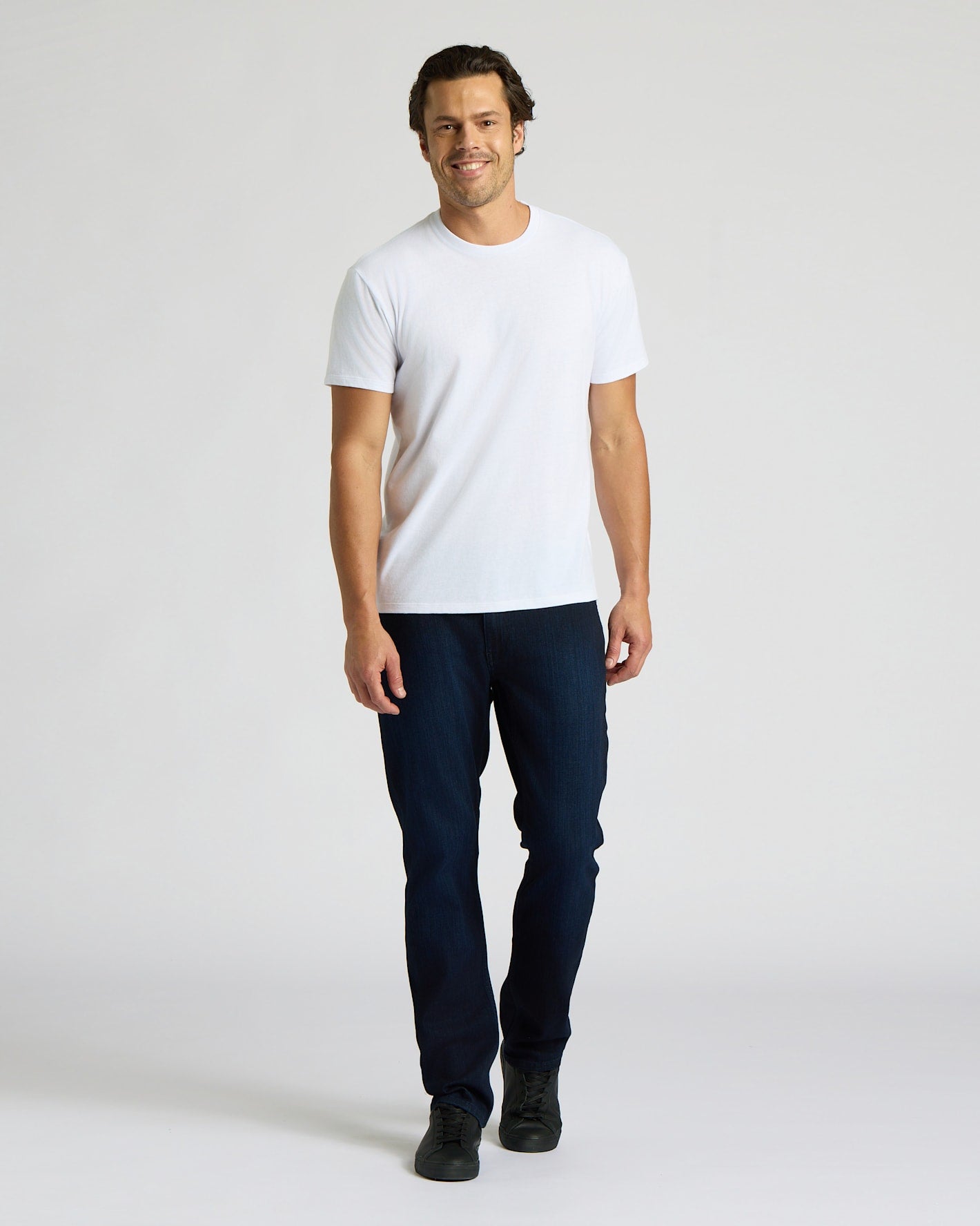 Man wearing a white t-shirt and dark jeans on a plain background