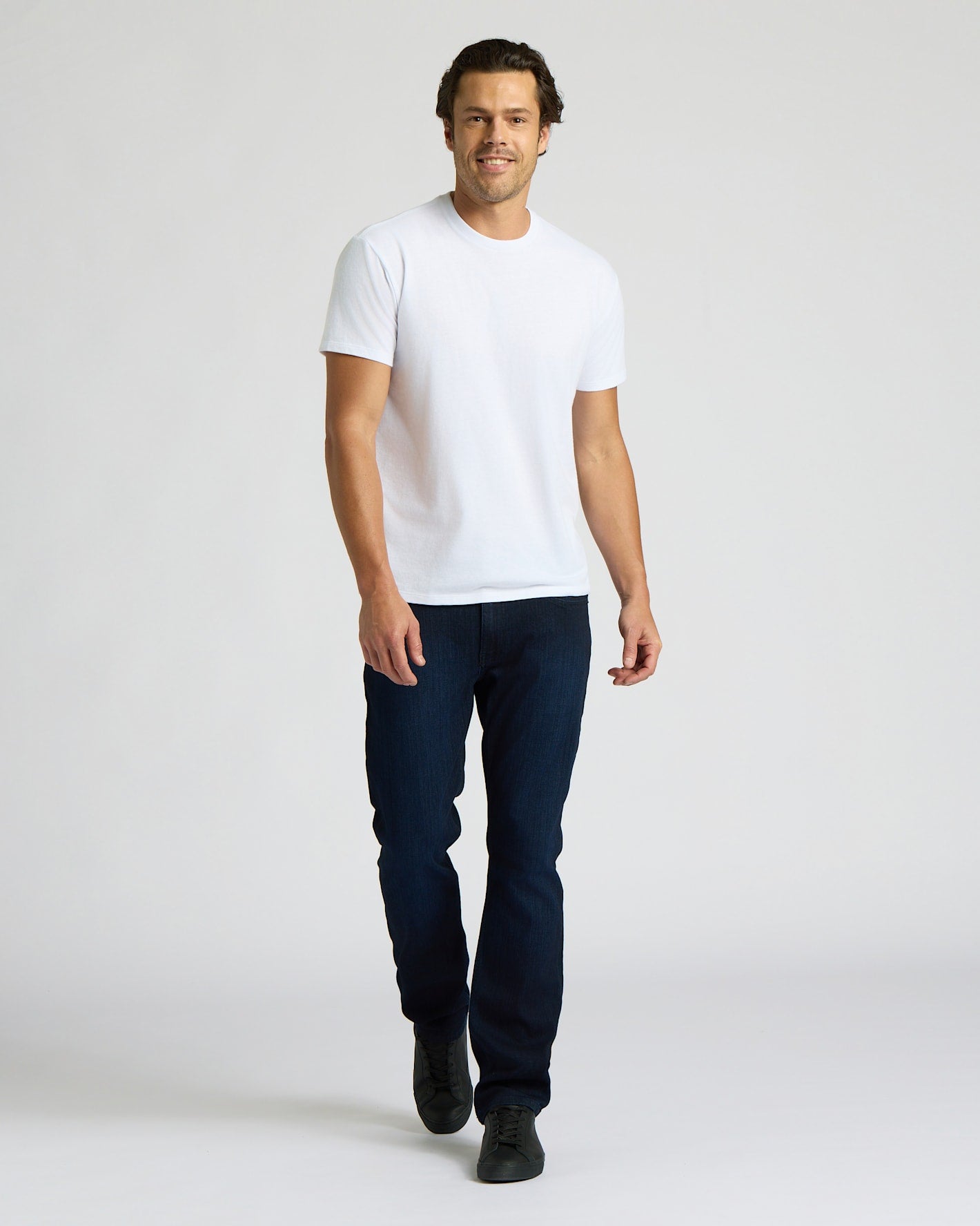 Man wearing a white t-shirt and dark jeans on a plain background
