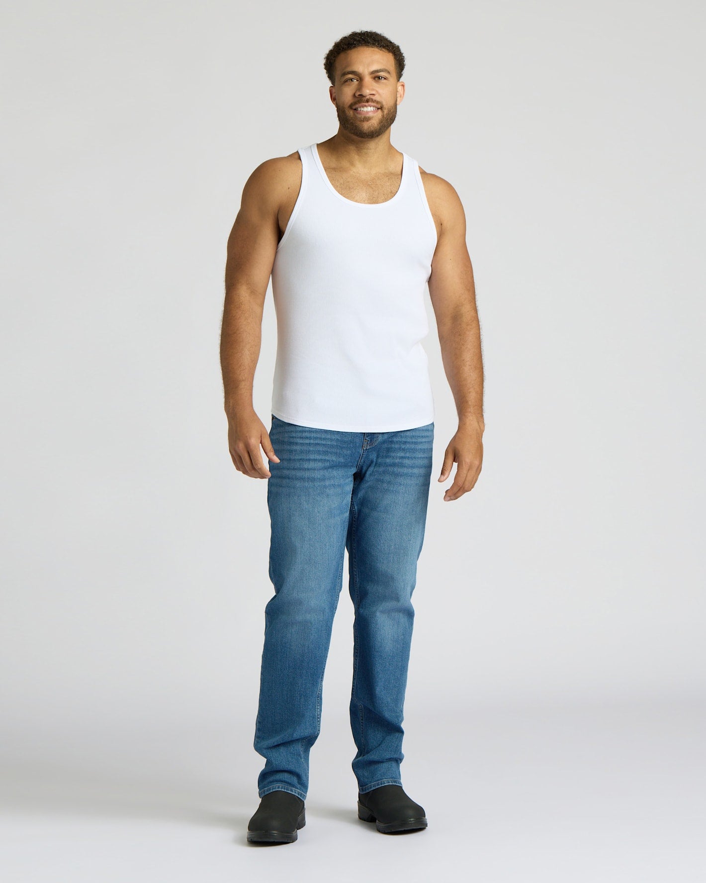 Man wearing a white tank top and blue jeans on a white background