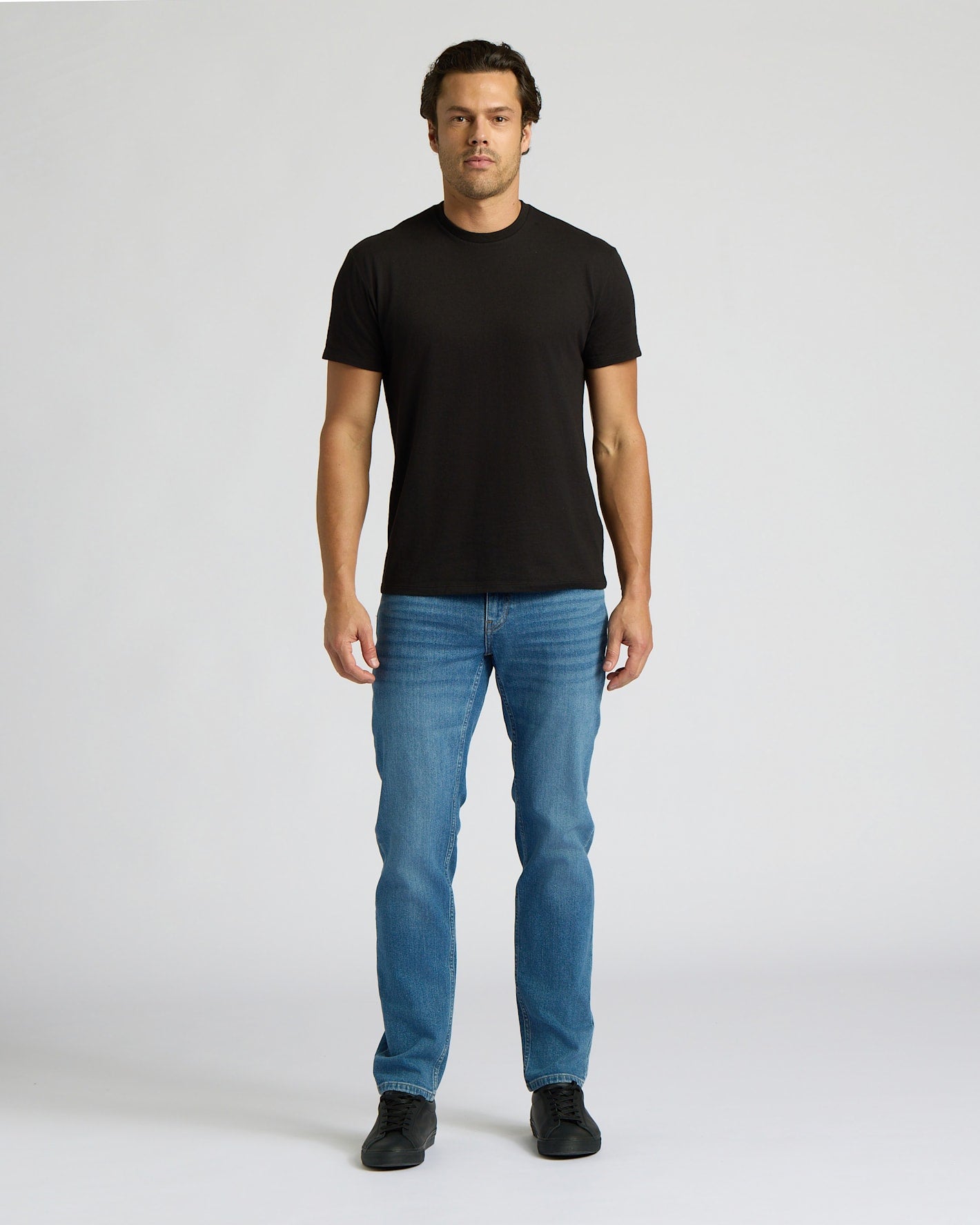 Man wearing a black t-shirt and blue jeans on a white background