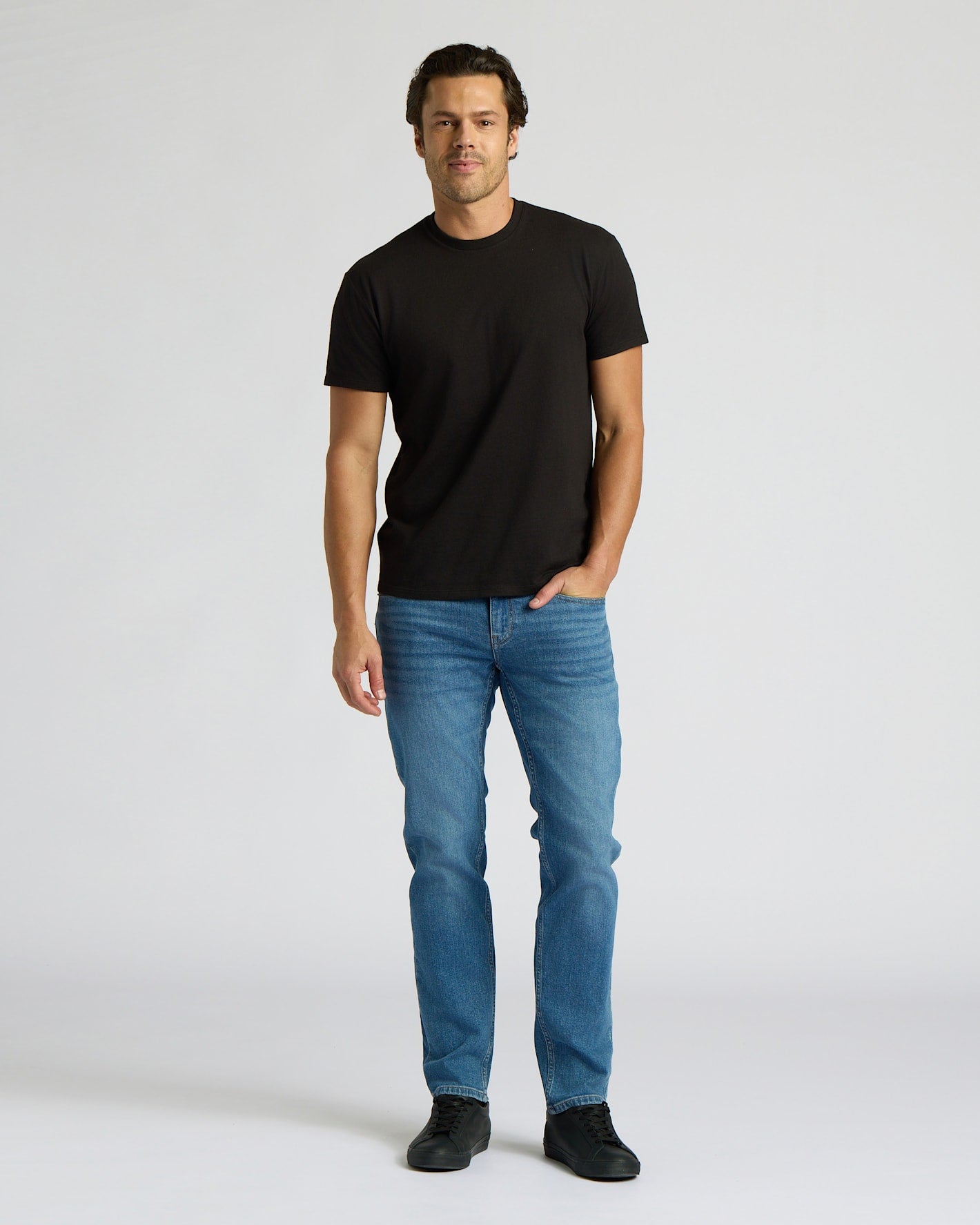 Man wearing a black t-shirt and blue jeans on a white background