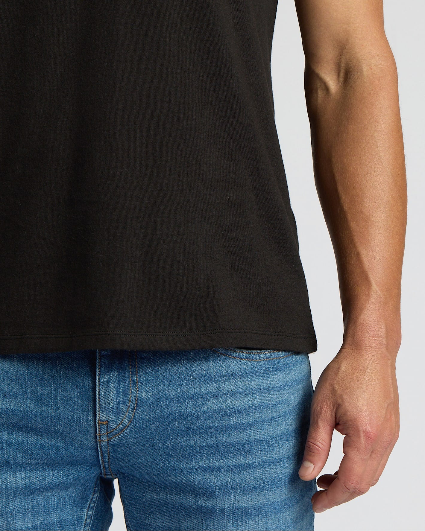 Person wearing a black t-shirt and blue jeans on a plain background