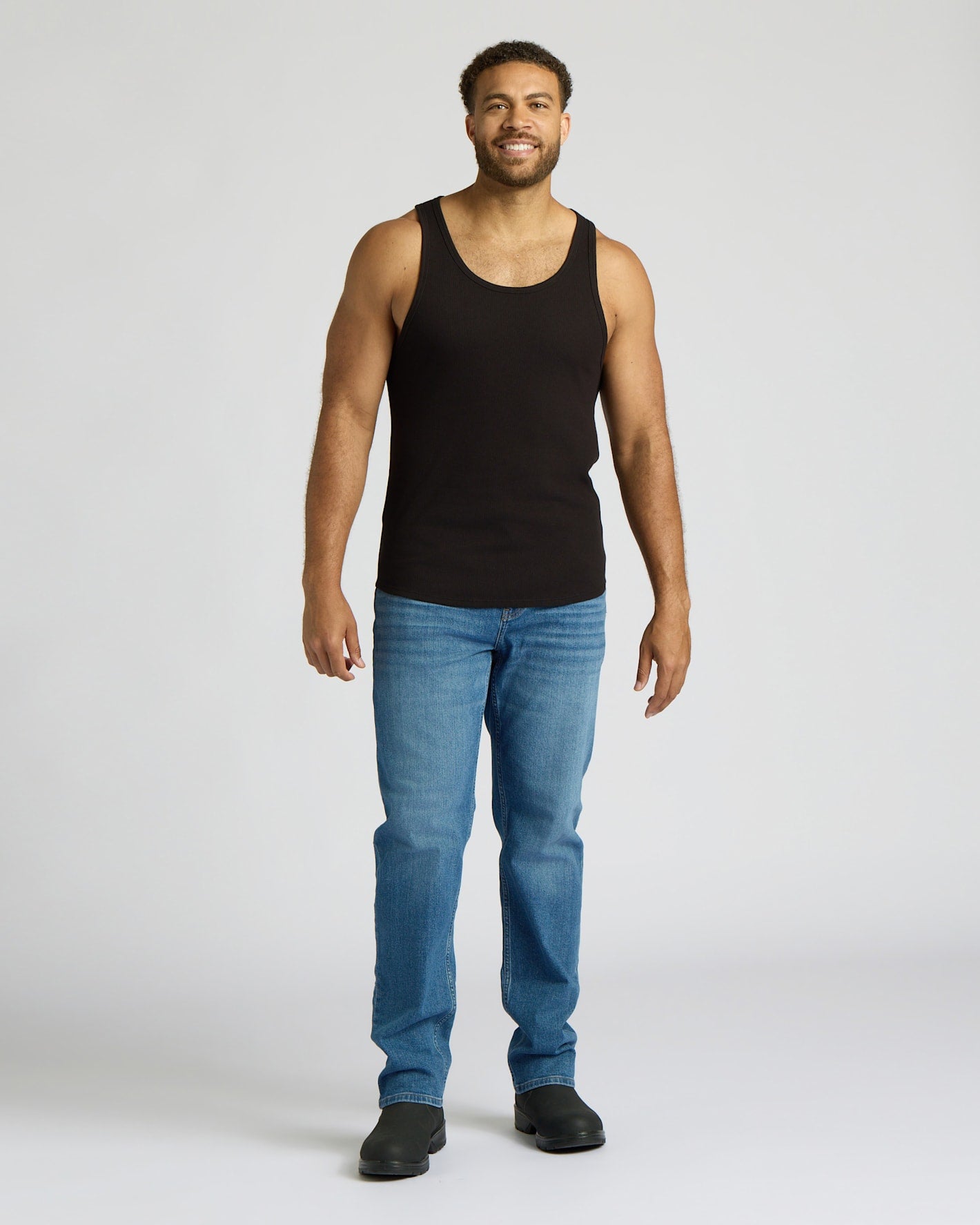 Man wearing a black tank top and blue jeans on a white background
