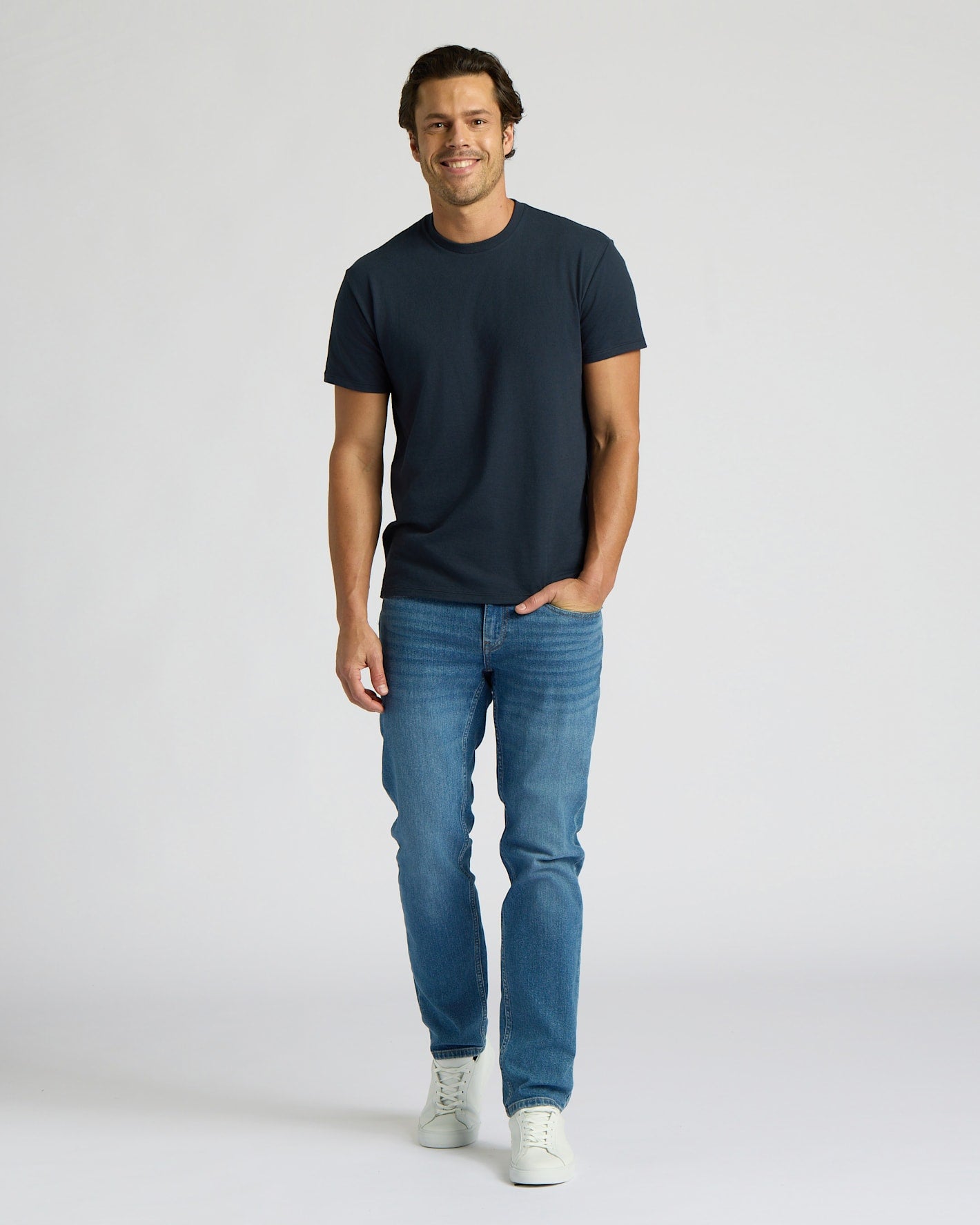 Man wearing a navy t-shirt and blue jeans on a white background