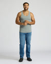 Man wearing a gray tank top and blue jeans on a white background