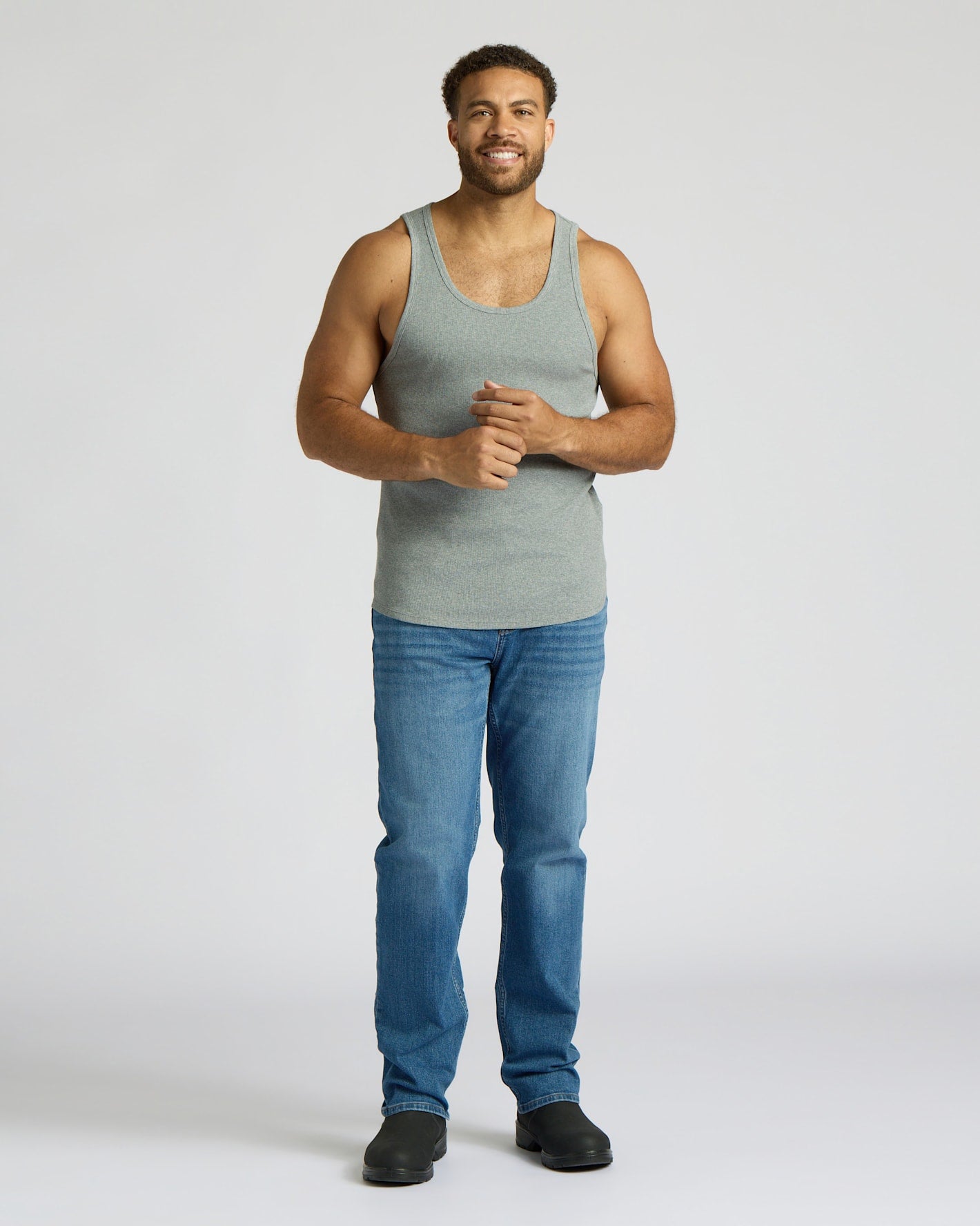 Man wearing a gray tank top and blue jeans on a white background