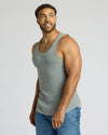 Man wearing a green tank top and blue jeans on a light gray background