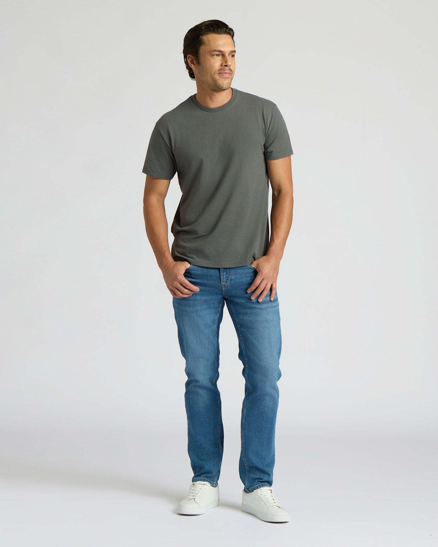 Man wearing a gray t-shirt and blue jeans on a white background