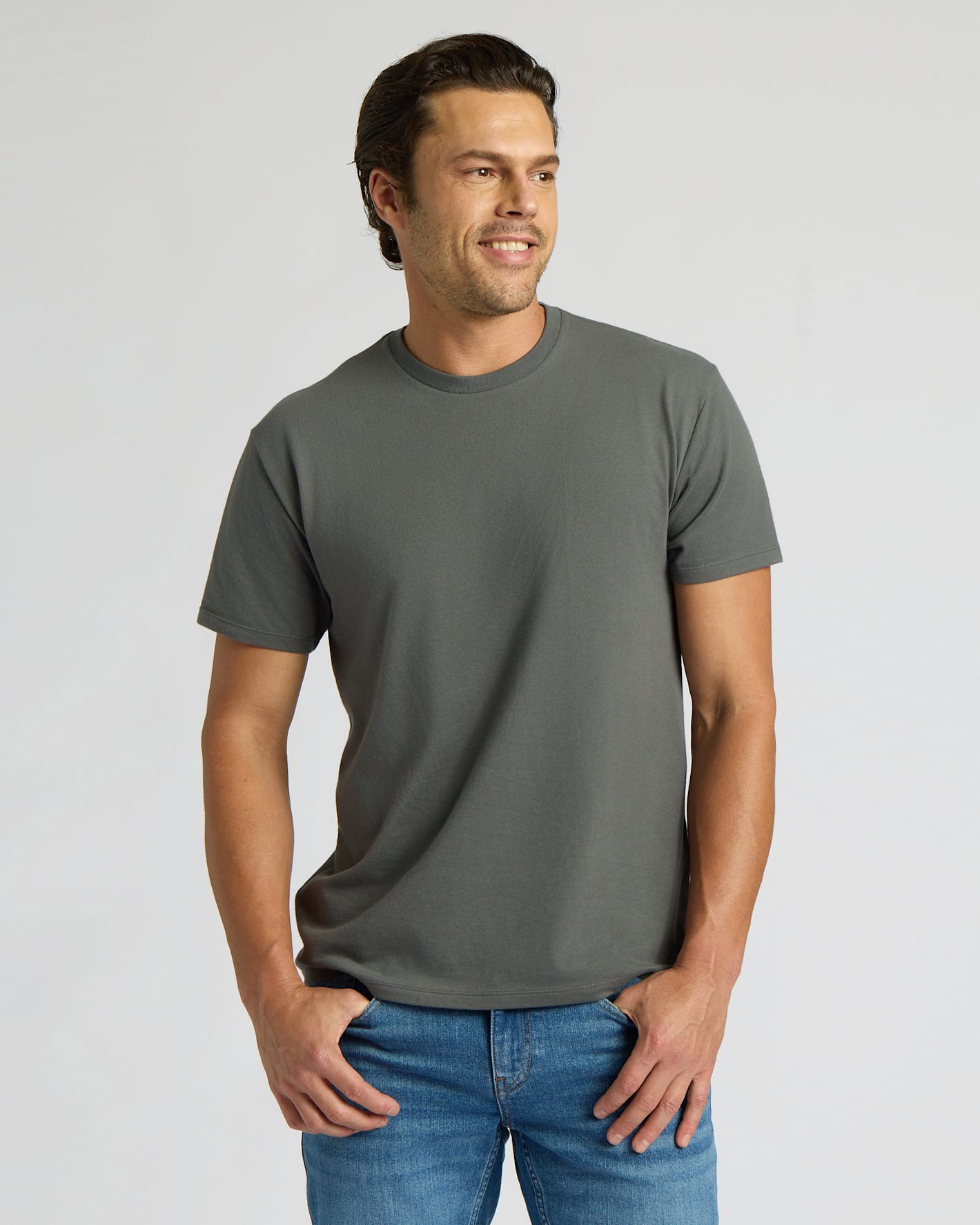 Man wearing a gray t-shirt and blue jeans on a light gray background