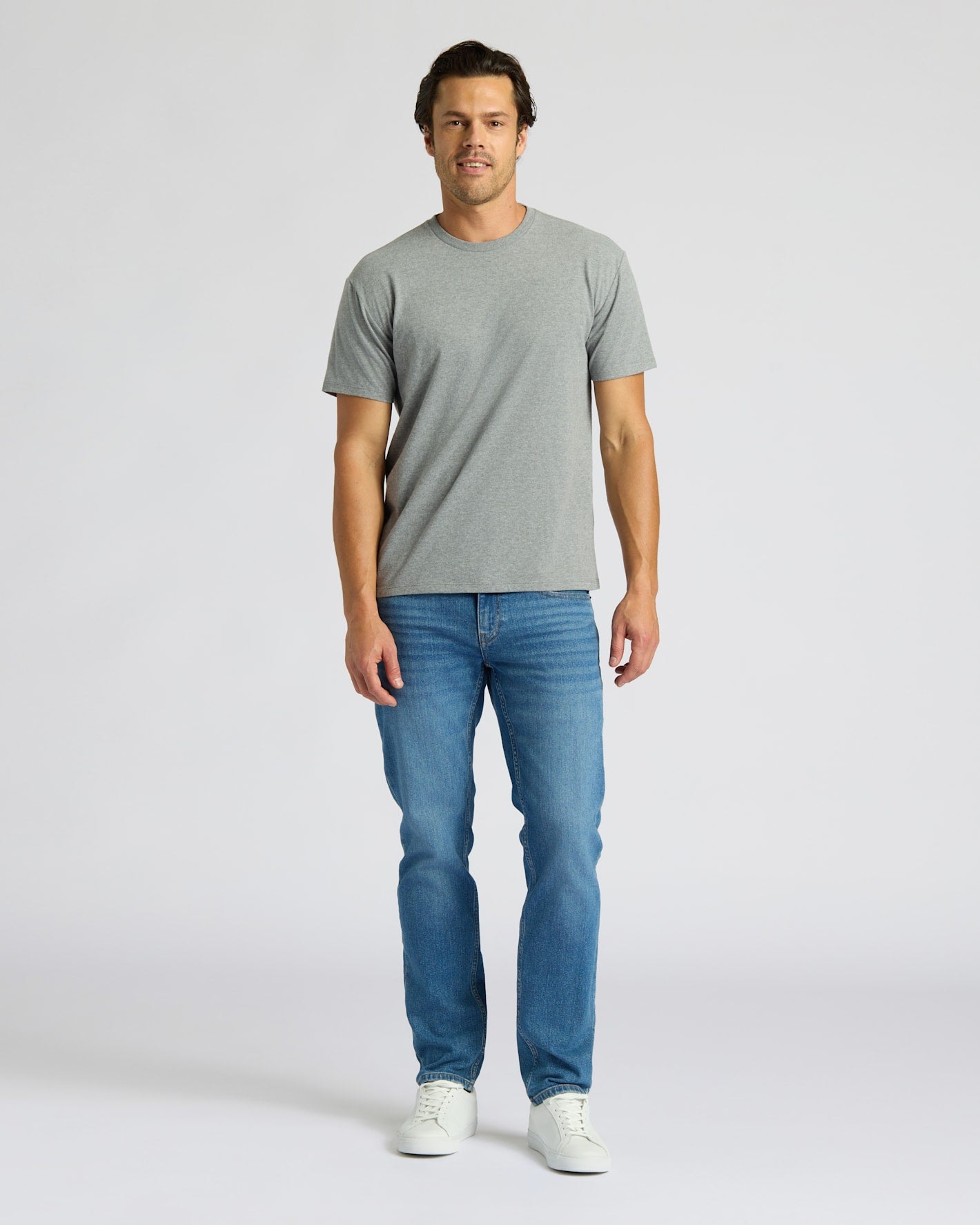 Man wearing a gray t-shirt and blue jeans on a white background