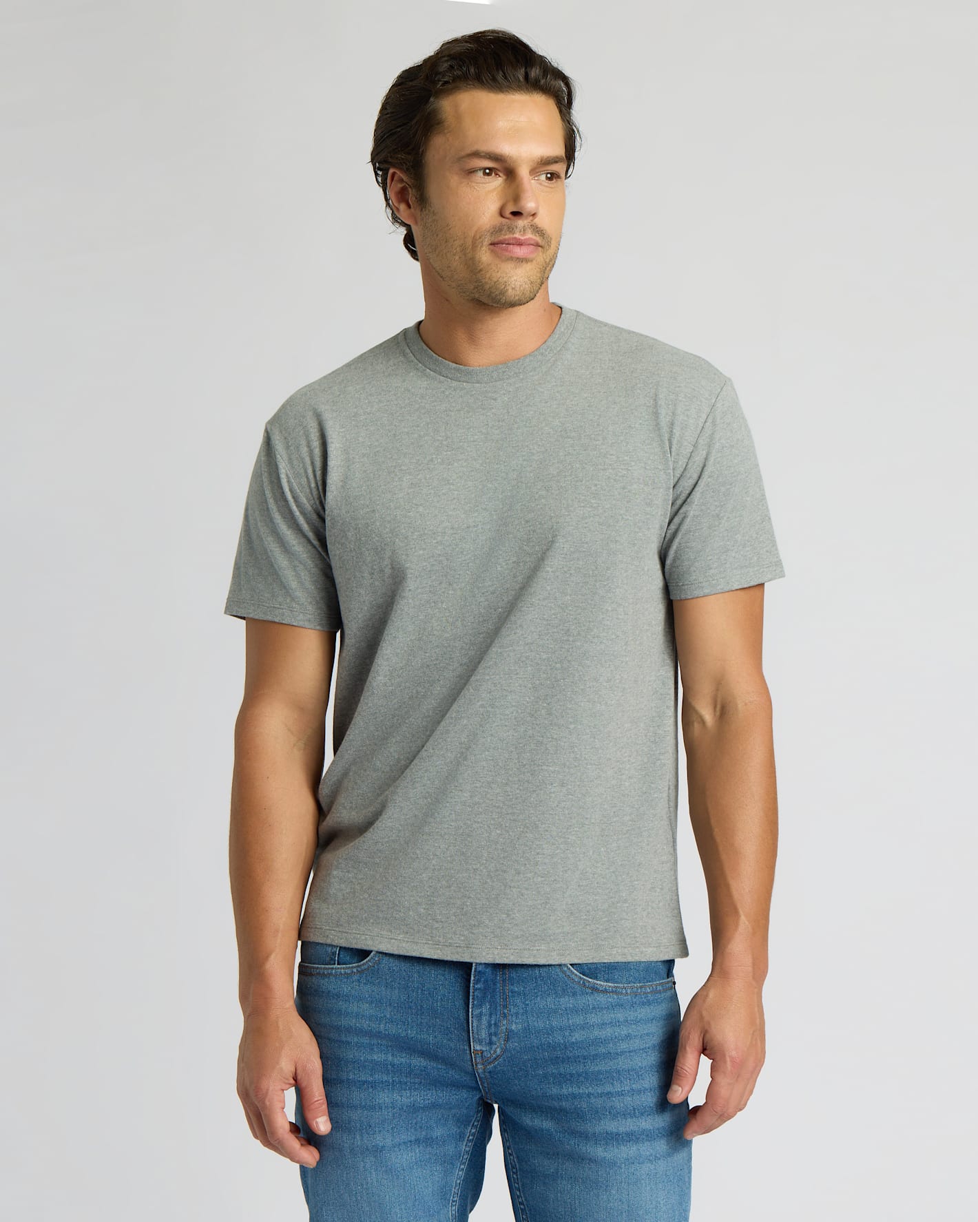 Man wearing a gray t-shirt and blue jeans against a plain background