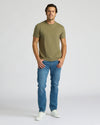 Man wearing an olive green t-shirt and blue jeans on a white background