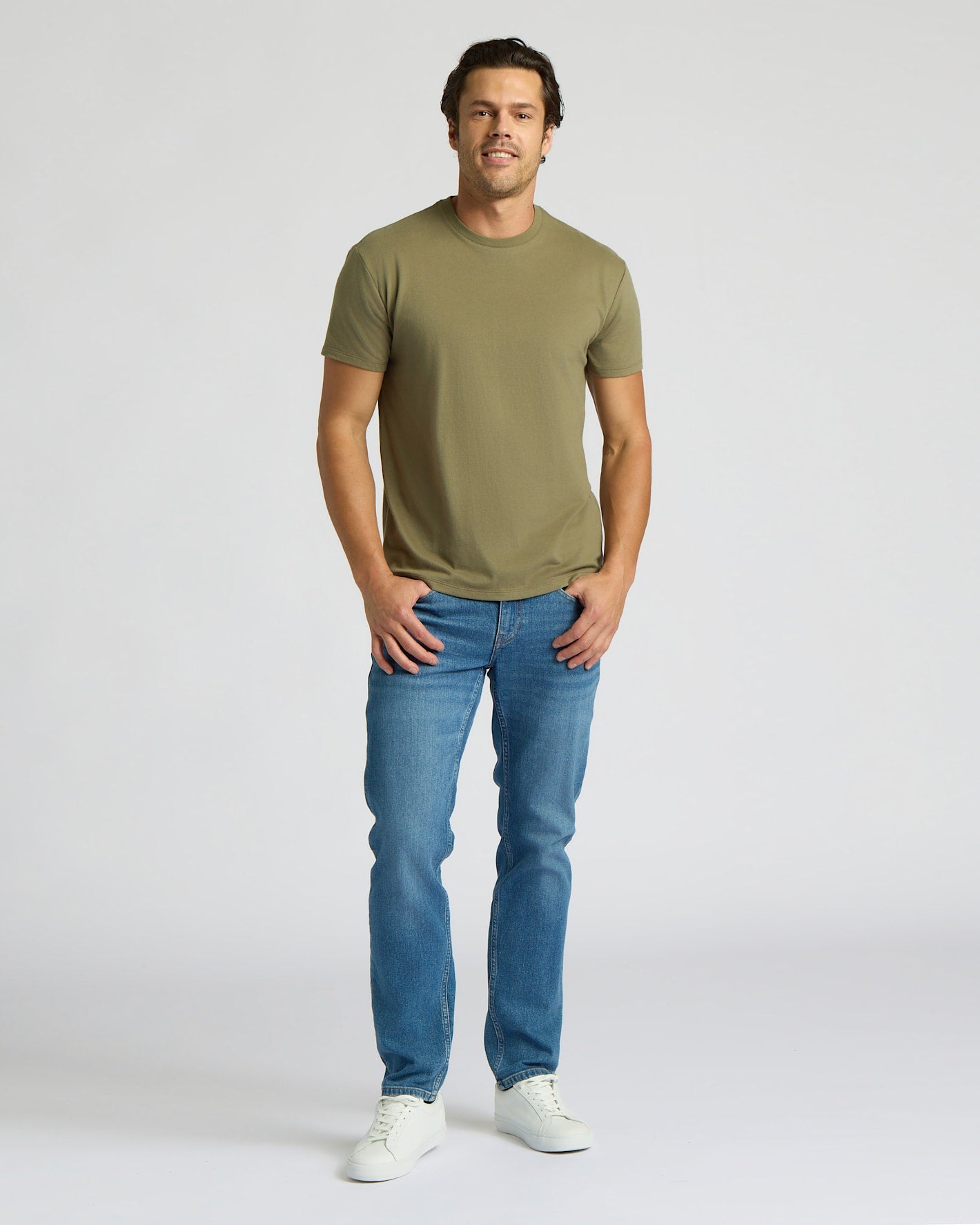 Man wearing an olive green t-shirt and blue jeans on a white background