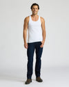 Man wearing a white tank top and dark jeans on a plain background