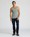 Man wearing a gray tank top and dark jeans on a white background