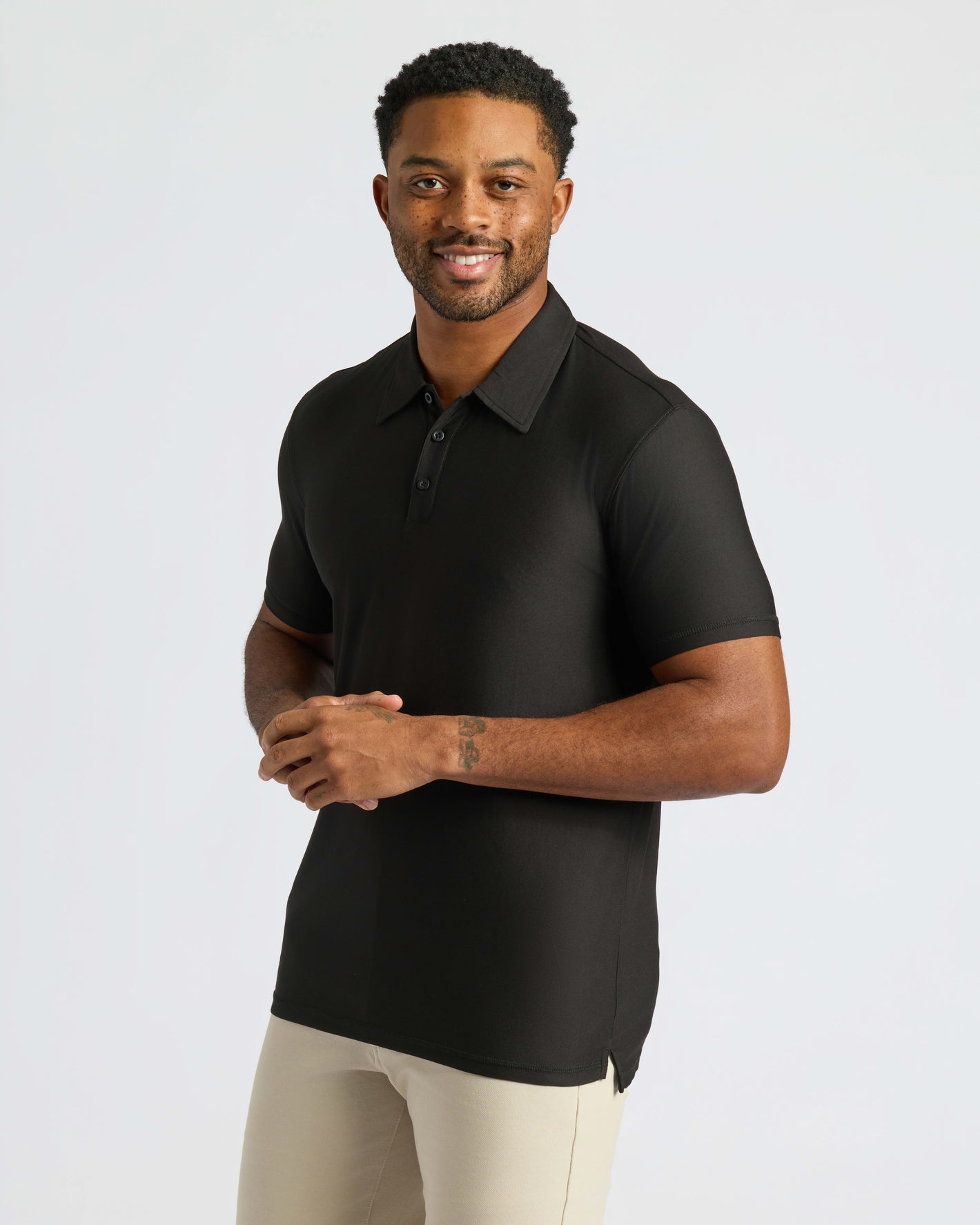 Man in Active Polo 10-Pack wearing black polo and beige pants.