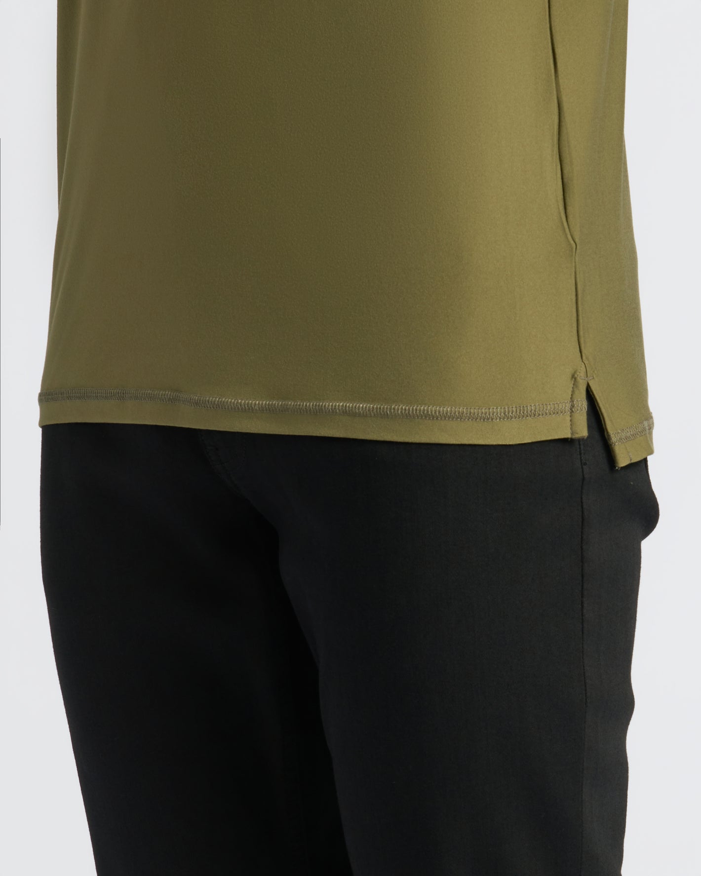 Military Green Active Polo 2.0 hem with side slit over black pants.