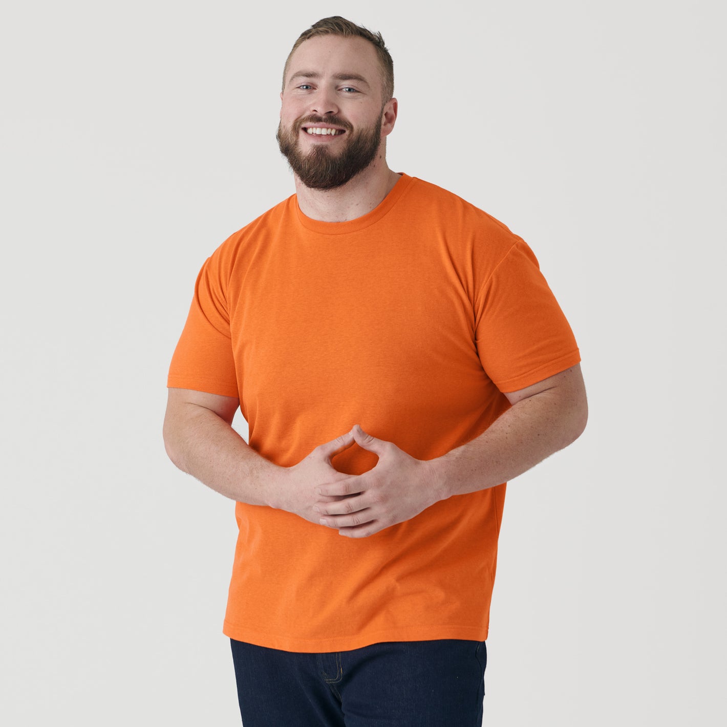 Man wearing Orange Short Sleeve Crew Neck Tee, smiling, hands clasped.