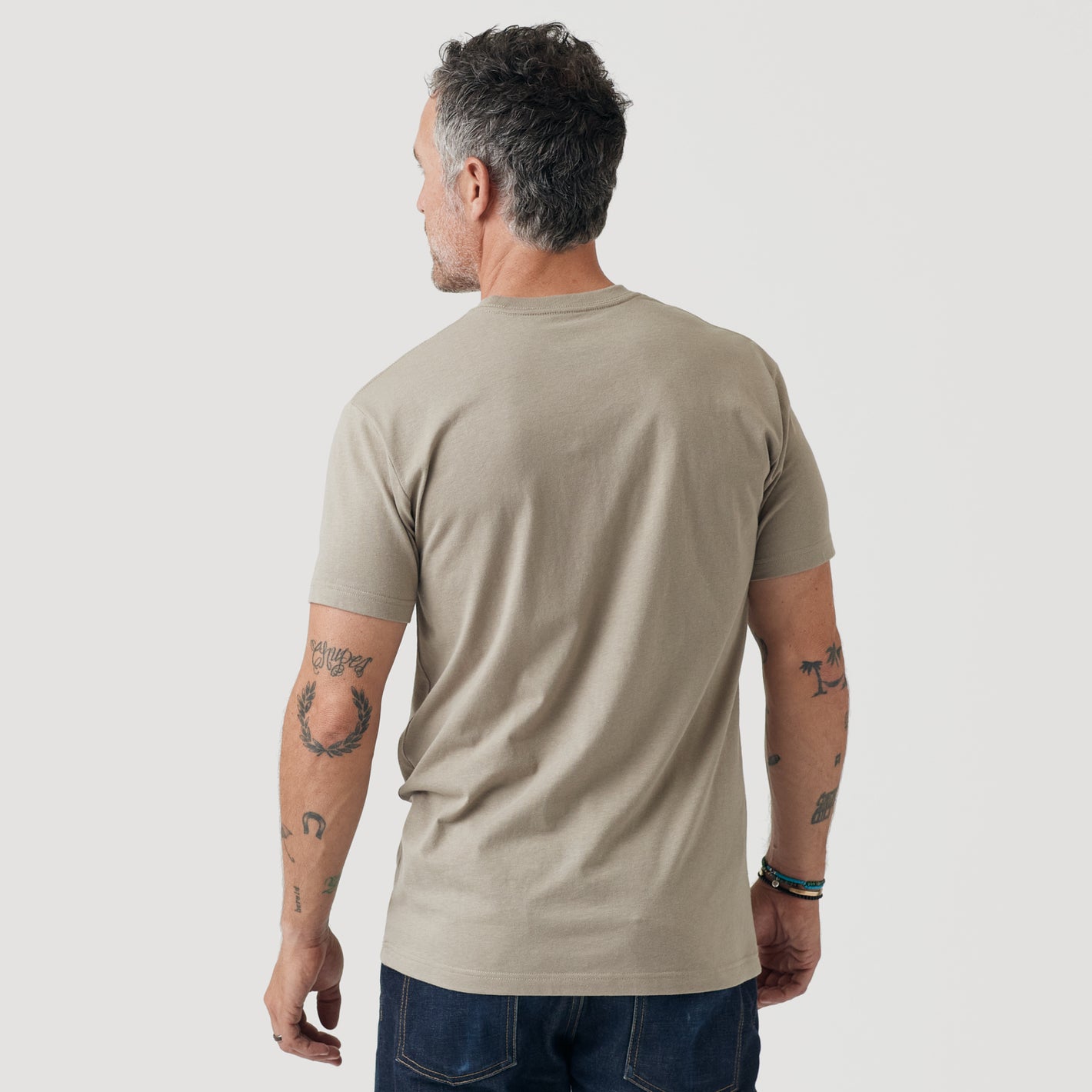 Man wearing Military Beige Short Sleeve Crew Neck Tee, showcasing tattoos and bracelets.