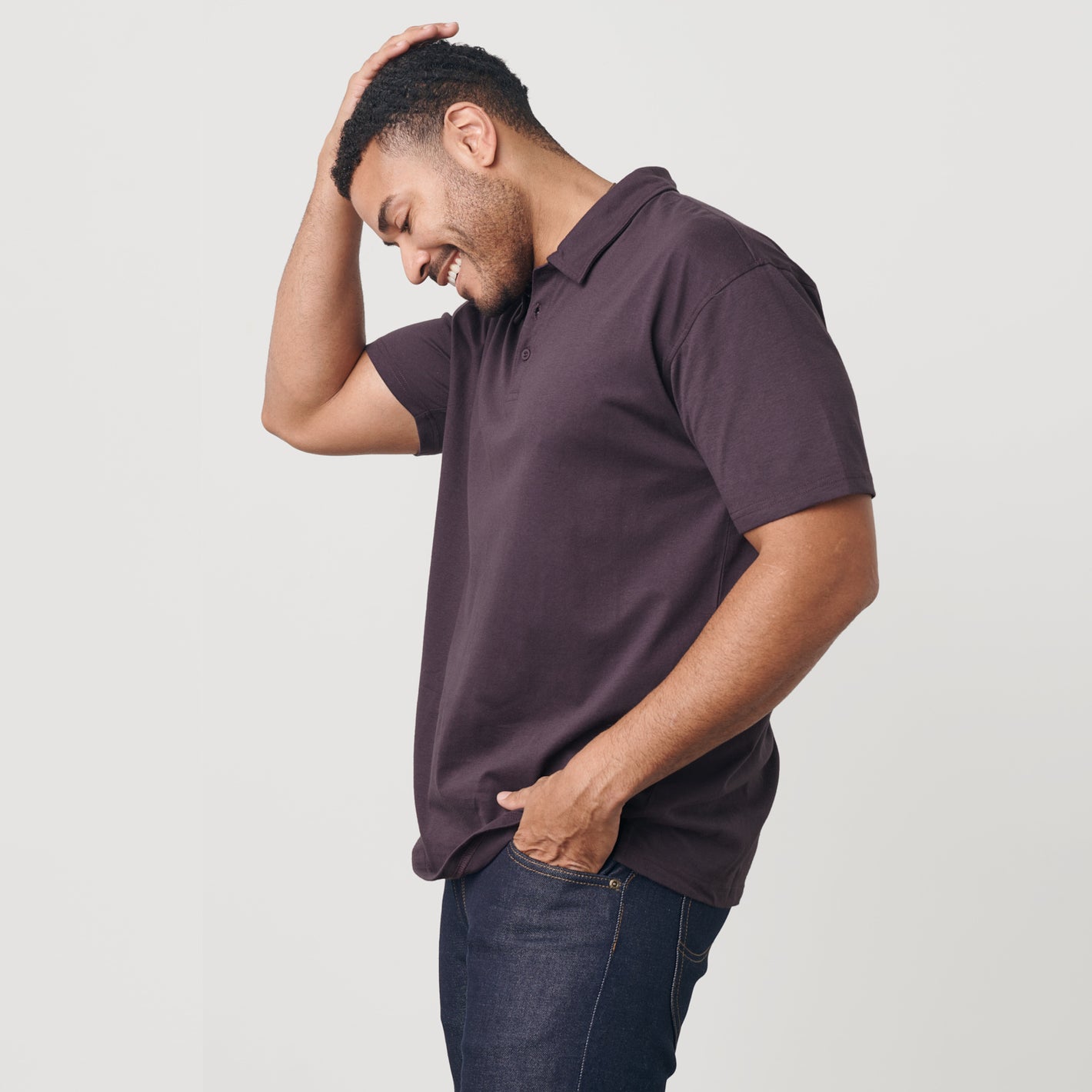 Man wearing Dark Purple Short Sleeve Polo, smiling with hand in pocket.