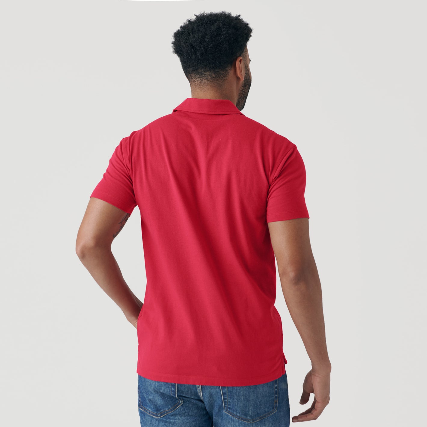 Man wearing Raspberry Classic Polo, blue jeans, seen from behind.
