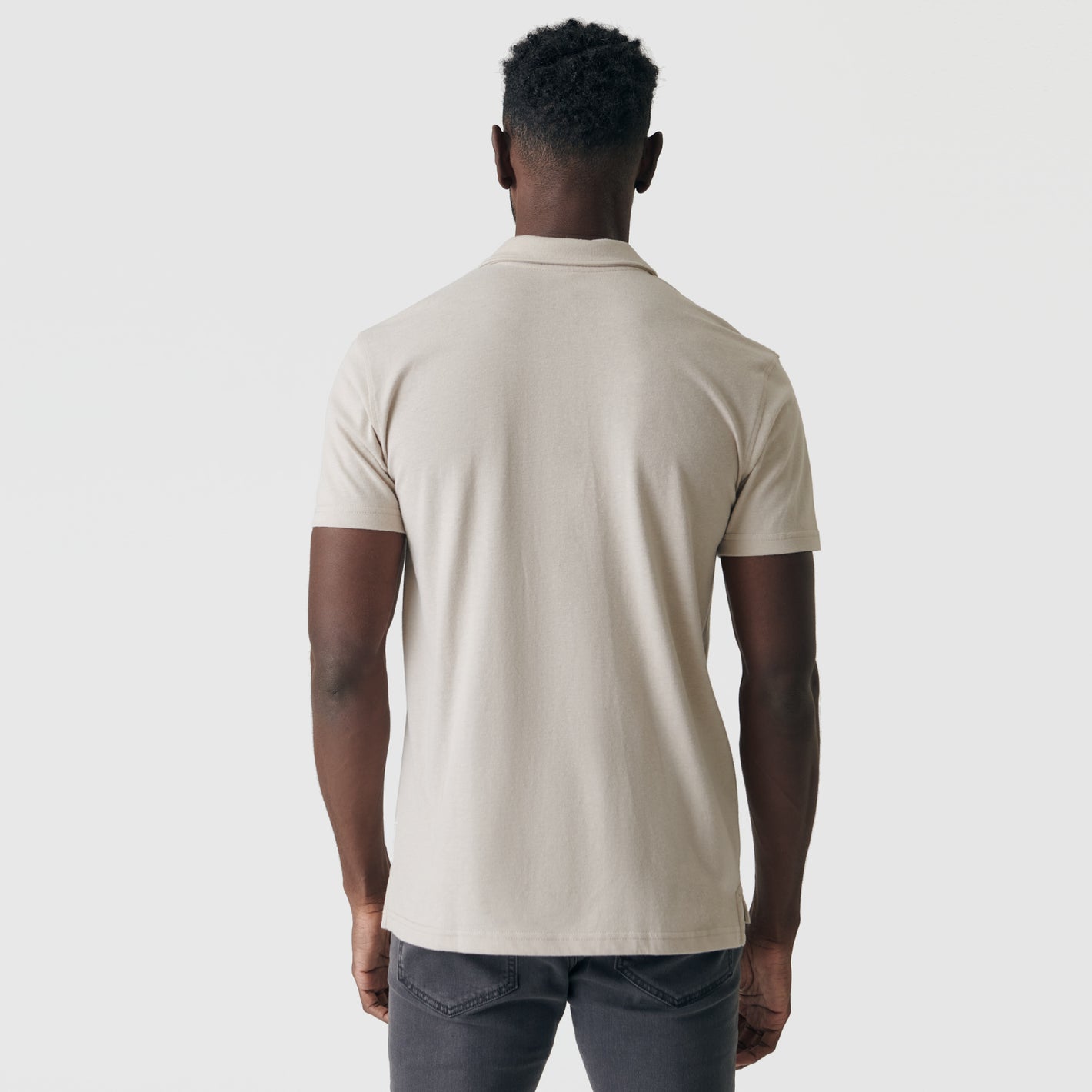 Man in Sandstone Classic Polo, back view, showcasing fit with dark gray jeans.