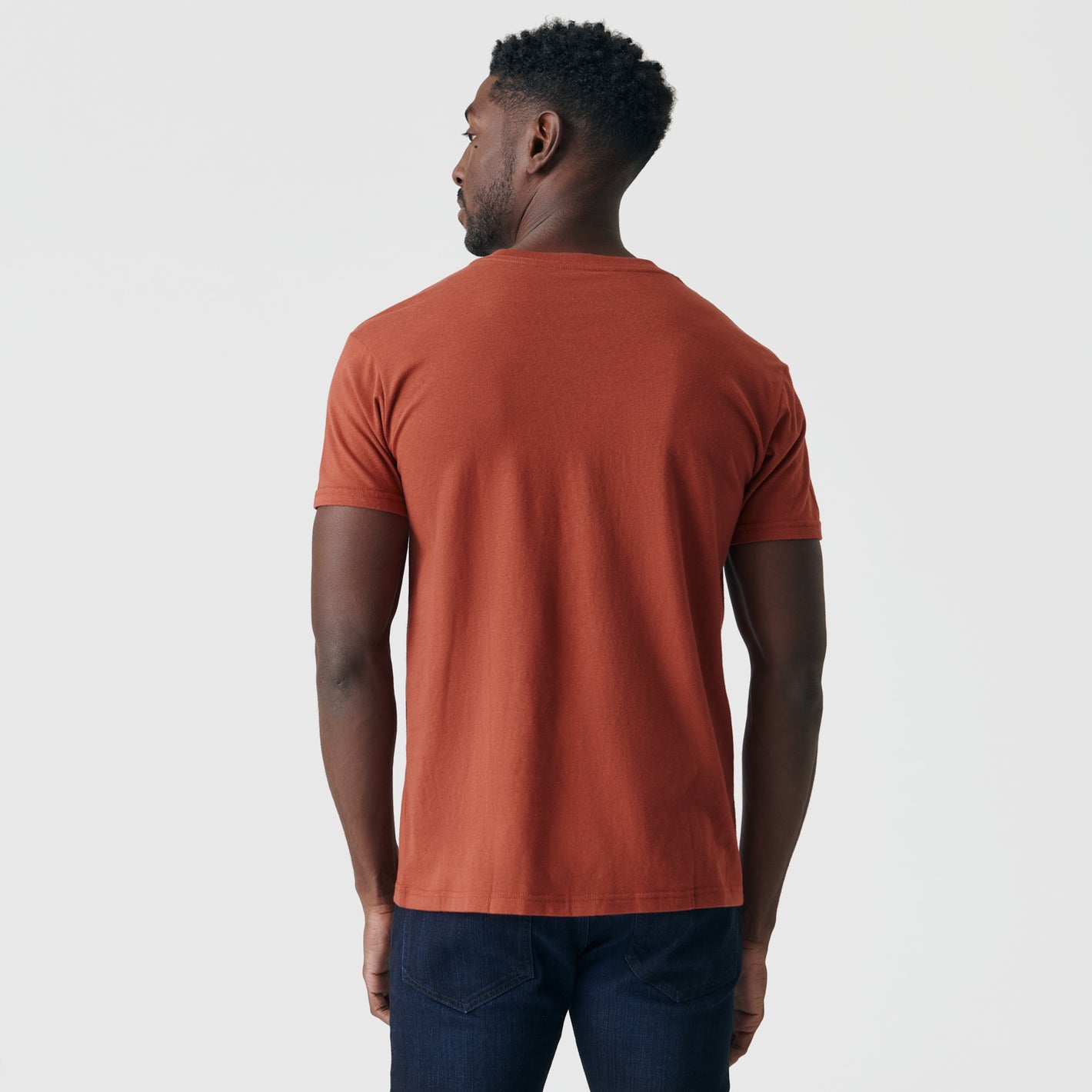 Man wearing Rust V-Neck Tee, back view, arms relaxed.