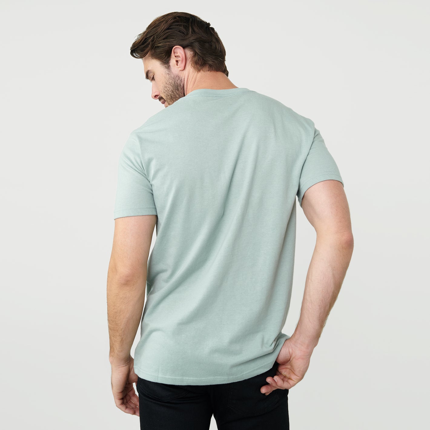 Man wearing Sage V-Neck Tee, viewed from behind, with black pants.