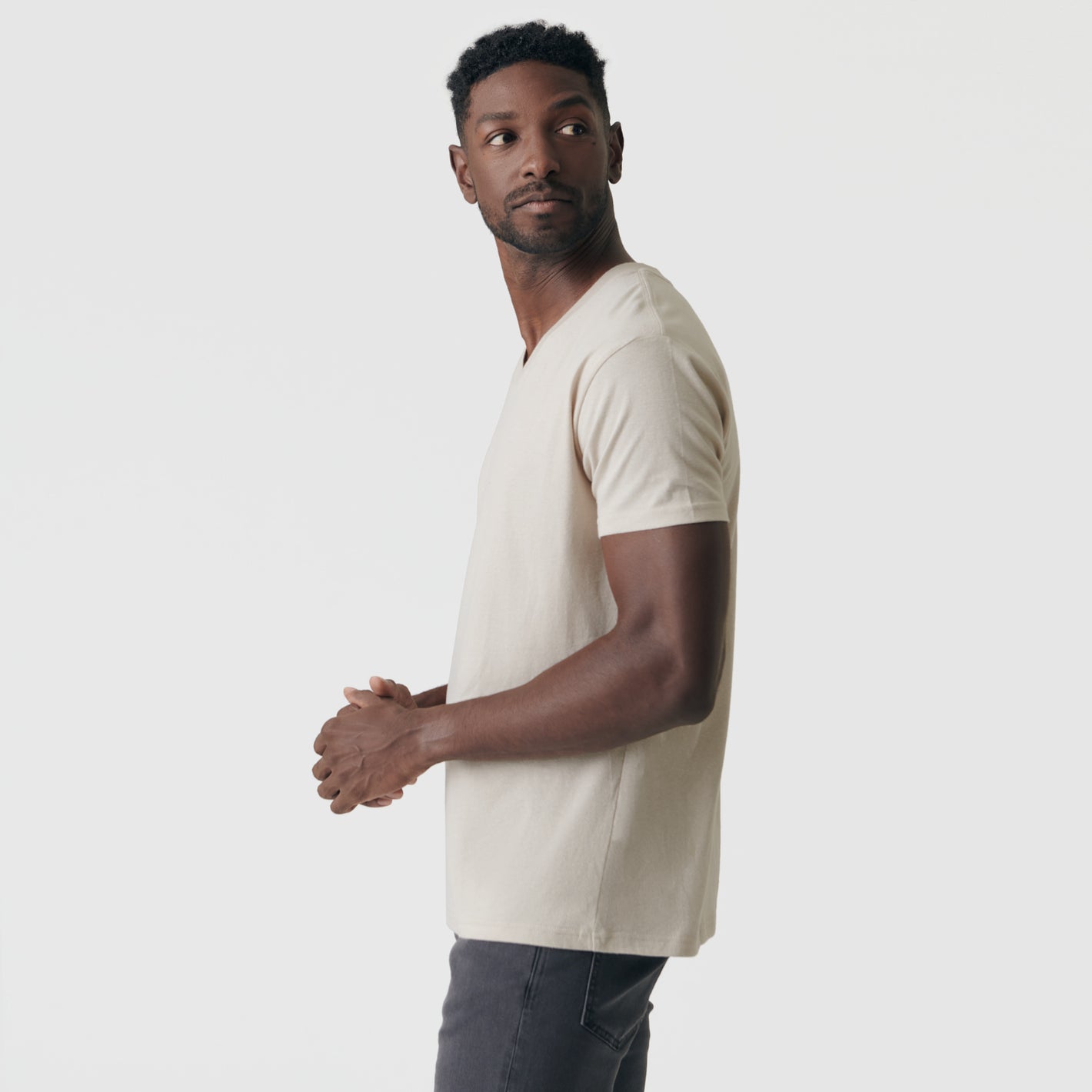 Man wearing Sandstone V-Neck Tee and dark gray jeans.
