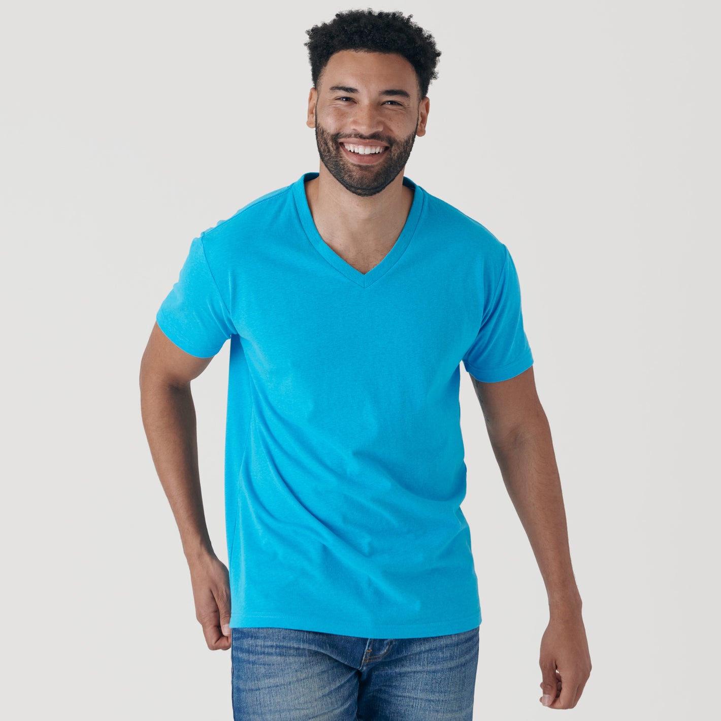 Man in Turquoise V-Neck Tee, smiling, with jeans.