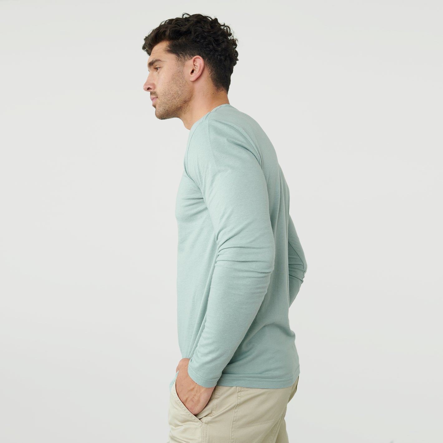 Man in Sage Long Sleeve Crew Neck Tee, hands in pockets, side view.