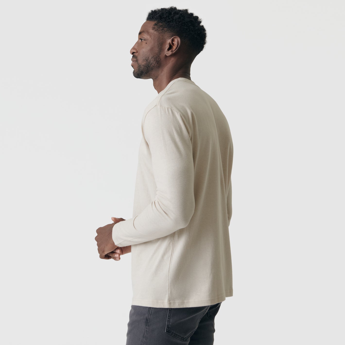 Man wearing Sandstone Long Sleeve Crew Neck Tee and charcoal jeans.