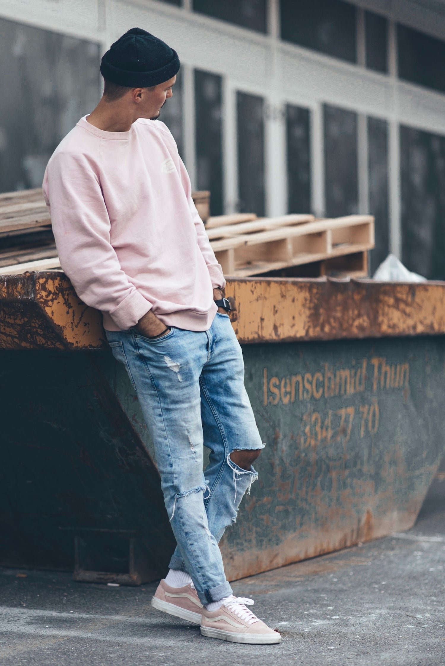 Model wearing a black beanie, pink sweatshirt, and torn jeans.