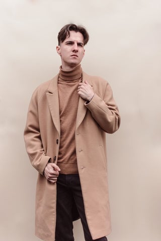 Model wearing a light brown overcoat with a matching colored turtleneck sweater underneath.