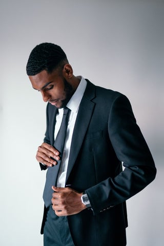 Model wearing a black blazer and matching tie along with a white dress shirt underneath.