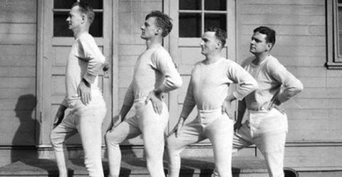 Old black and white photo of 4 men in a line in the same pose with the left hand on their hip wearing all white