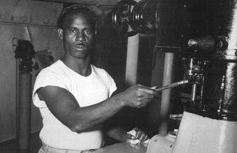 Old black and white photograph of man working on some pipes wearing a white t-shirt