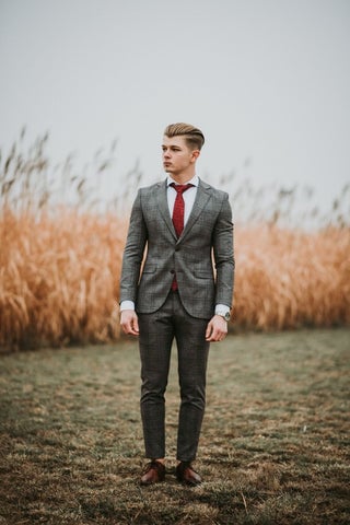 Model wearing a gray suit with a red tie and white dress shirt and brown dress shoes.