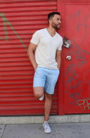 Man wearing True Classic White V-Neck T-Shirt and blue shorts in front of red building