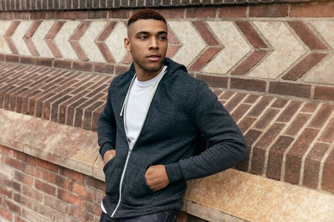 Man wearing True Classic Carbon Fleeced French Terry Zip Hoodie leaning back on a brick wall